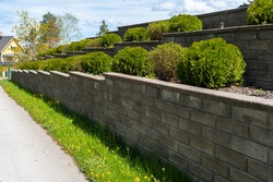 Garden landscape design. Decorative wall made of dark gray stone blocks or concrete cement bricks. Garden decorative trimmed shrubs or bushes are fenced with rocky stones masonry.