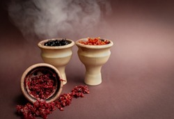 Three hookah bowls with aromatic tobacco on a brown table with smoking accessories. Hookah smoking in a hookah lounge. Red, yellow, black hookah tobacco