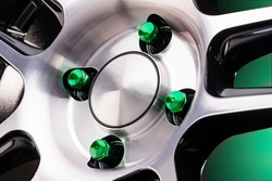 beautiful bright automotive wheel heptahedral nuts green close-up on a sporty style alloy wheel on a black background for auto tuning of a tire and disk store or auto parts gradient green background