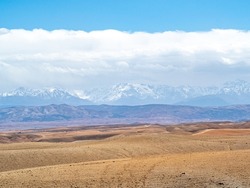 Agafay Desert with Atlas Mountains in background with blue skies and fluffy white clouds.