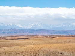 Agafay Desert with Atlas Mountains in background with blue skies and fluffy white clouds.