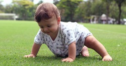 Cute one year old baby exploring grass outside at park, toddler boy touching grass