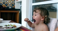 Toddler boy eating lunch with spoon. Little baby infant eats meal by himself