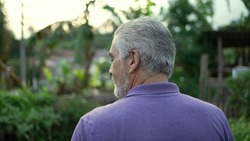 Back of contemplative senior man walking forward in nature. Pensive older person walks outdoors in contemplation