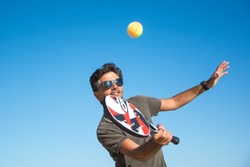 Man Holding A Paddle Tennis Racket Hitting The Ball On A Blue Background. Young Sportsman Playing Tennis On The Beach. Paddle Player