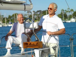 Two senior men at steering wheel of sailing boat in marina