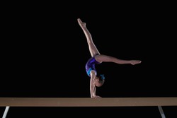 Young female gymnast performing handstand on balance beam, side view