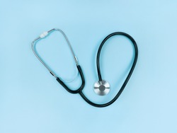 Black stethoscope on a soft blue background. Simple flat lay.