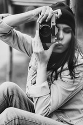 portrait of a beautiful hipster girl in a cap and a denim jacket with a camera taking photos outdoor
