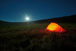 Illuminated with orange light tourist tent at night. Overnight stay of tourists on a moonlit night