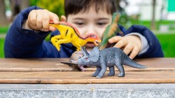 cute kid is playing with  dinosaurs toys on park bench, spring, green nature, grass. happy dinosaur day, may 15 and june 1. fascinating dinosaur fantasies. spring outside, public park,having fun.