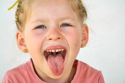 Cheerful smile child. Girl laughs close-up of the face on a white background. little girl show tongue, throat. portrait with wide open mouth and protruding tongue. clear view pulls out long tongue. 