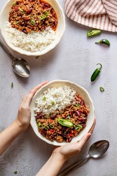 Two bowls on the table with chilli con carne, with hands holding one plate, top view, with fresh jalapeno peppers 