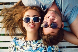 Close up portrait of happy smiling couple in love laying in wood white floor. Wearing retro clothes and sunglasses. Reflection of palm trees in glasses.