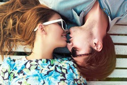 Happy young couple laying on white floor and have a sweet kiss, wearing retro clothes and sunglasses.