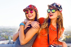 Best friend having fun on the roof, going crazy together, wearing floral swag hats and mirrored sunglasses, amazing view on the city, bright colors evening sunlight.