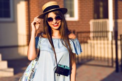 Young pretty hipster cheerful girl posing on the street at sunny day, having fun alone, stylish vintage clothes hat and sunglasses, travel concept , young photographer with vintage camera.
