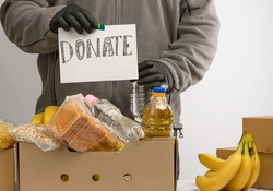 man holds a sheet of paper with a lettering  donate and collects food, fruits and things in a cardboard box to help the needy and the poor, the concept of help and volunteering