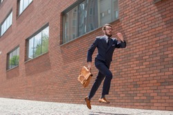 Young businessman with a briefcase and glasses running in a city street on a background of red brick wall