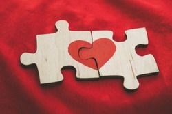 Red heart is drawn on the pieces of the wooden puzzle lying next to each other on red background. Love concept. St. Valentine day
