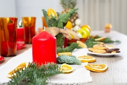 The Christmas festive table is decorated with candles, Christmas tree branches, dried oranges, beautiful bright dishes, sweets and fruits, selective focus 