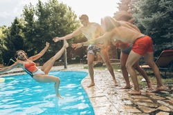 A young group of friends jumping into the swimming pool.Having fun and refreshing on a hot summer day.A young group of friends jumping into the swimming pool.Having fun and refreshing on a hot summer 