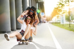 Two female friends playing with skateboard.One girl pushing other from behind.Laughing and fun.