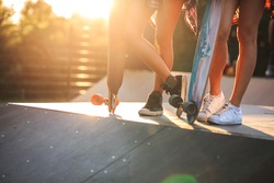 Two female friends standing with skateboards at the skate park.Only legs and boards are visible.Sunset.