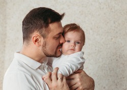 A gentle portrait of a young father and baby daughter on a bright background. Tenderness, parenthood