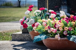 Cemetery in sunny day. Gravestone with flowers and candles. Grave decoration close-up. Graveyard in the daytime. Grave flowers in pot.