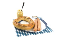 a large Hamburg pretzel and two Vienna sausages on a blue plate and a jar of Parisian mustard isolated on white