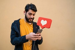 Portrait of young latin man using his mobile phone. Red heart like notification. Social media and communication concept.