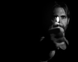 A grayscale portrait of an adult male holding a lighter in front of his face against a dark background