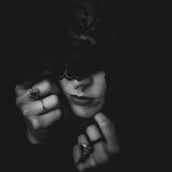 A grayscale shot of a woman with a covered face wearing many rings and holding beads