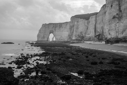 
A beautiful rocky beach near the French city of Etretat with cliffs Falaise d'Aval. The photo is taken in black and white.                               