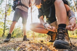 Close up of young female hiker tying shoelaces and getting ready for trekking in forest with man on background.