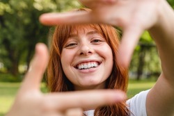 Smiling young ginger-haired student girl woman posing on selfie photo looking at camera walking outdoors in park.