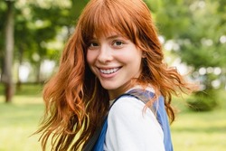 Close up portrait of a young caucasian woman girl teenager student schoolgirl with ginger red hair and toothy smile walking in park forest outdoors looking at camera.