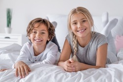Happy time concept. Brother and sister lying in bed at the morning and smiling in camera. Boy and girl siblings playing relaxing on the bed.