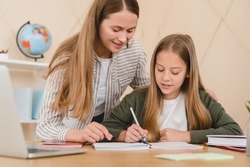 Young caucasian teacher mother tutor babysitter nanny helping her daughter schoolgirl student with homework, school project, preparing for test exam at home.