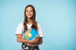 Caucasian young teenager schoolgirl pupil student holding hugging globe on geography lesson isolated in blue background. Happy Earth day!