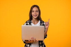 Cutout teenager schoolgirl holding laptop computer showing pointing on copy space having idea, surfing webpages on Internet, social media posting,e-learning remotely isolated in yellow background