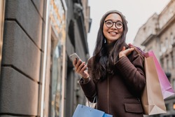 Asian woman using smartphone and looking away while enjoying a day shopping. Black friday, sale and discount. Buying clothes presents for holidays
