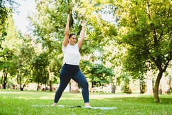 Slimming burning calories exercises. Caucasian plump young woman athlete in fitness clothes doing yoga on fitness mat outdoors in park.