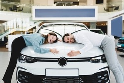 Extremely satisfied happy caucasian young couple family husband and wife hugging embracing their new car, feeling excited after buying expensive auto at auto dealer shop store.