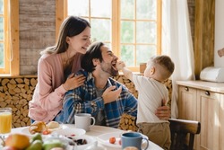 Funny family moments together. Morning breakfast with parents and little toddler kid child infant feeding father with cake at home kitchen. Parenthood and adoption