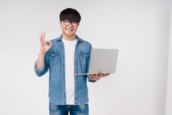Asian korean young coder programmer student man freelancer hacker working remotely on laptop, doing online shopping, e-learning on distance, browsing showing okay isolated on white background