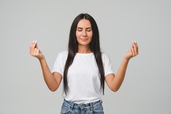 Serene people concept. Relaxed concentrated caucasian young woman girl meditating praying to God, doing yoga isolated in grey background. Zen-like stress relief exercises