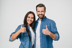 Confident young caucasian couple man and woman husband and wife spouses boyfriend and girlfriend showing thumbs up looking at camera isolated in white background. Quality check