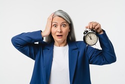 Deadline! Hurry up! Scared mature middle-aged businesswoman CEO freelancer manager in formal suit holding alarm clock watch feeling shock isolated in white background